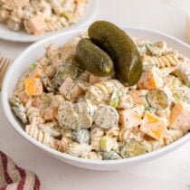 Creamy dill pickle pasta salad with cubes of cheddar cheese, pickle slices, and rotini pasta, topped with whole pickles.