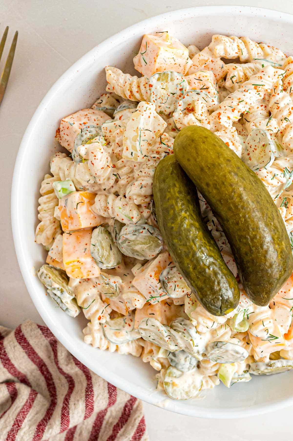 Overhead view of creamy dill pickle pasta salad with rotini, cheese cubes, sliced pickles, and whole pickles on top.